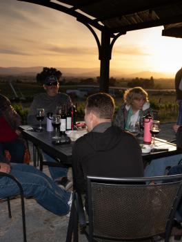 group of people sit at a table with wine at sunset