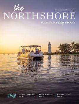 A boat with passengers cruises calm waters of The Northshore at sunset, heading toward a historic lighthouse, capturing a serene travel moment.