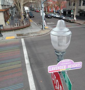Photo of a lamppost and street sign with the name Lavender Heights, standing above a rainbow crosswalk