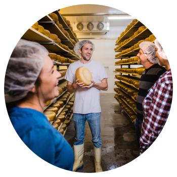 Cheesemaker Shep holding a cheese wheel with visitors in the aging room