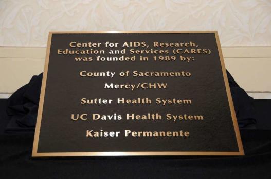 A photo of a bronze plaque with the words Center for AIDS, Research, Education, and Services (CARES) was founded in 1989 by the County of Sacramento, Mercy/CHW, Sutter Health System, UC Davis Health System, Kaiser Permanente