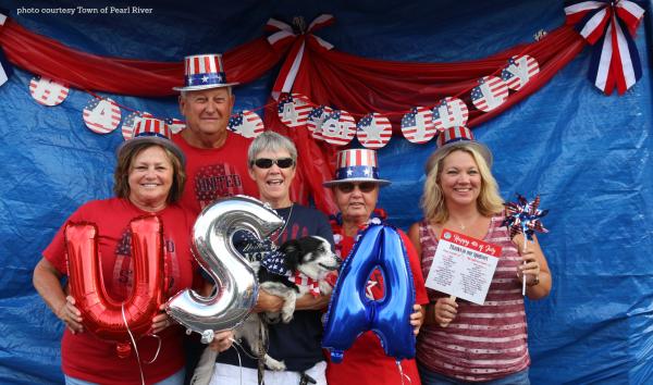 Patriotically dressed men and women hold USA balloons in front of red, white and blue bunting at the Pearl River 4th of July Celebration