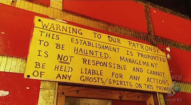 A yellow sign that reads, Warning to Our Patrons. This Establishment is purported to be HAUNTED. Management is NOT responsible and connato be held liable for any actions of any ghosts/spirits on this premesis