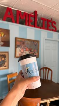 A person holding a cup of coffee in a to-go coffee cup with Amelie's written on the holder