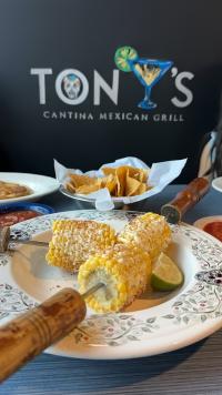 delicious Mexican street corn (Elote) on a plate, garnished with a lime wedge, and accompanied by a side of crispy tortilla chips."