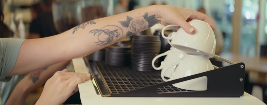 a ladies tatooed arm reaching for a coffee cup from a stack of them