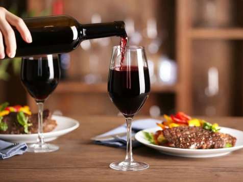 Hand pouring red wine for two, with two entrees on the table.