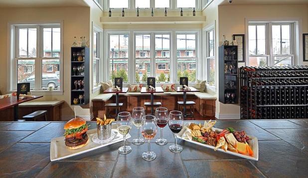 Wine glasses, a plate filled with fruit and cheese, and a plate with a burger and fries stand on a stone bar