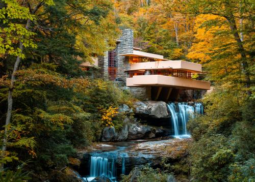 Iconic architectural building Fallingwater sits atop a waterfall with fall foliage surrounding.