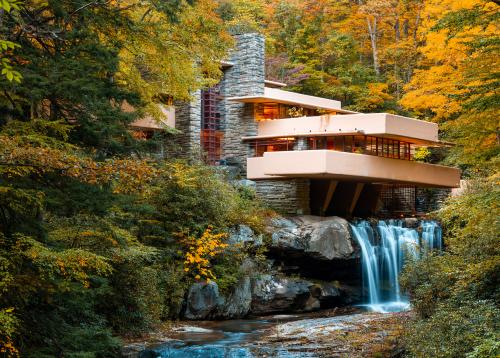 Iconic architectural building Fallingwater sits atop a waterfall with fall foliage surrounding.