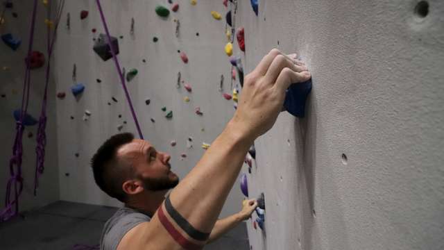 A man looks for his next handle while climbing the wall at Bliss Climbing and Fitness