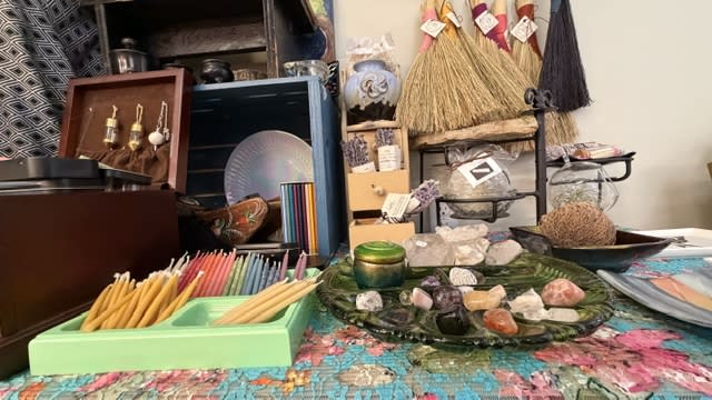 A table full of jewelry, Knick knacks, and candles sit on a table with a floral tablecloth.