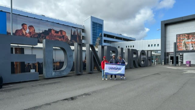 American Footgolfers standing in front of a large Edinburgh sign, holding a Lansing Sports Commission sign.