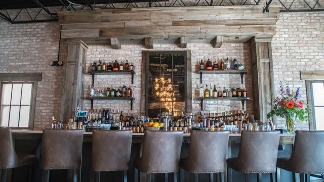 Seneca bar area with stools lined up in front of bar and exposed brickbehind the bar with shelving and bottles