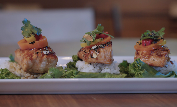 Image of three pieces of salmon placed on top of rice and lettuce. The three pieces of salmon are lined up in a row.