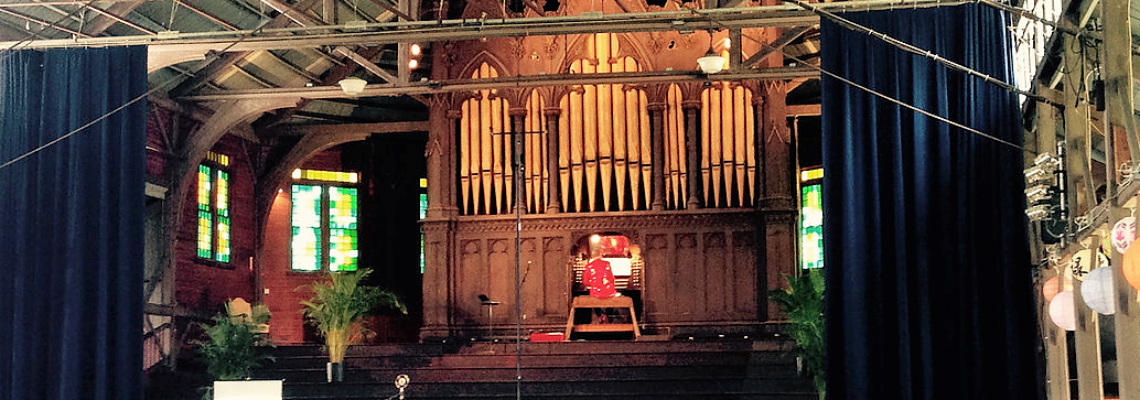 Man sitting at the large organ on stage with his back to the audience