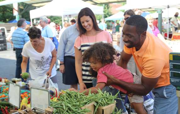 Man holding a little girl up while she selects fresh produce from the Bloomington Community Farmers Market