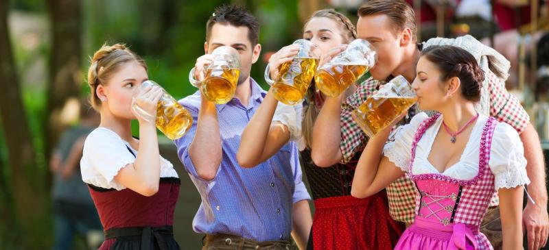 Group of five 20-somethings - three women dressed in German garb and two men in modern clothes - drink beer from large glass steins at OMNI Brewing Co's Oktoberfest