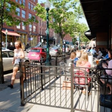 Groups of people sitting outside at a cafe down a tree-lined street in Armory Square in Syracuse