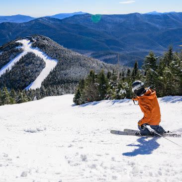 Skiier glides across snowy mountain, overlooking Adirondack Mountain peaks and snow-covered ski trails