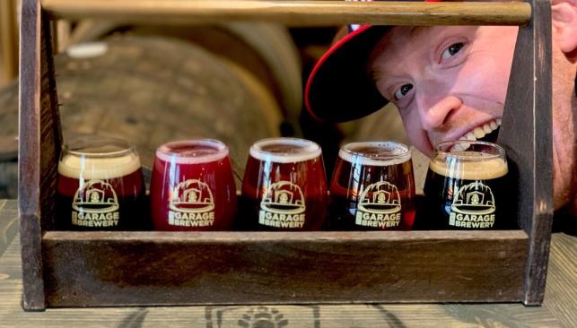 Smiling man behind a sampling of beer at The Garage Brewery