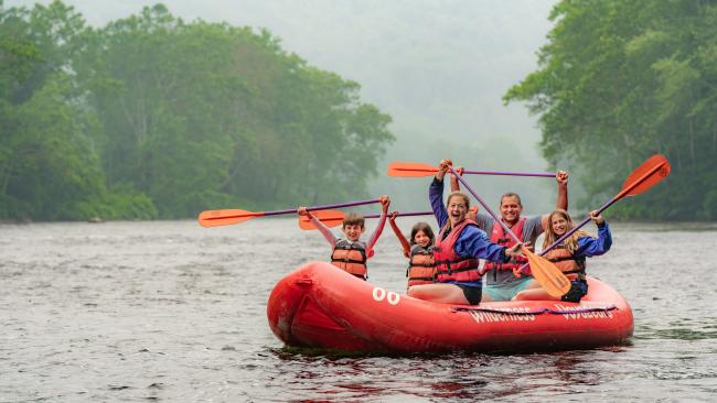 Family holds rafting paddles above their head while floating on a white water raft