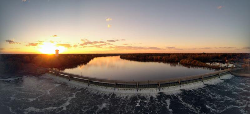 The sun sets over the horizon behind the dam and lake at Mississippi Gateway Regional Park