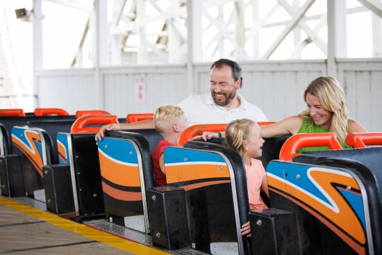 Family of four riding the Zippin Pippin Roller Coaster in Green Bay, Wisconsin at Bay Beach. Mom and daughter are sitting in the same row and father and son are sitting in the same row.