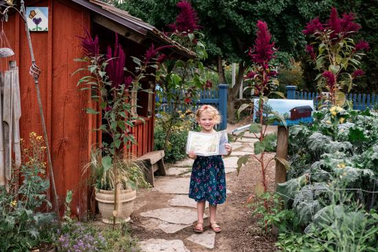 Young girl holding the map at the Bell Children's Garden in Green Bay, Wisconsin with the garden scenery behind her, smiling at the camera.