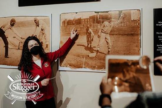 A woman in a red jacket points out old photographs at the Louisville Slugger museum.