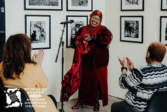 A woman in a red outfit stands singing to museum visitors.