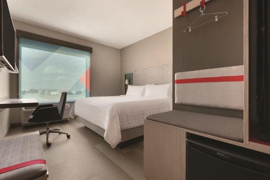 Guest room with a queen bed, desk, tv, mini-fridge and open closet space