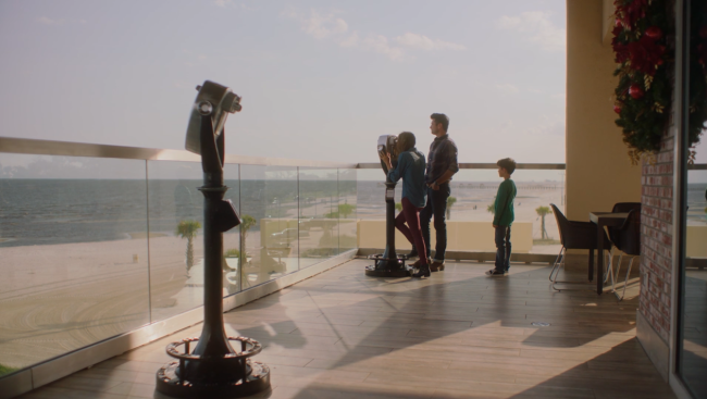 A picture containing three people standing on a balcony overlooking a beach.