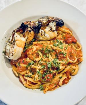 Two large shrimp sit on top of a plate of pasta smothered in tomato sauce and garnished with herbs at Piatto, Fort Smith, Arkansas.