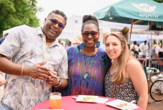 Three people stand at a table smiling at the Wine & Food Festival.