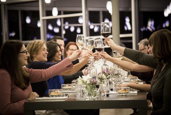 A group of people seated at a long dining table are raising their glasses for a toast.