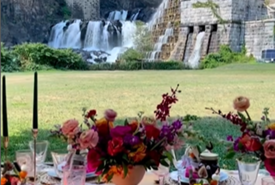 A picnic table with red and pink flowers is set up near the Croton Dam.