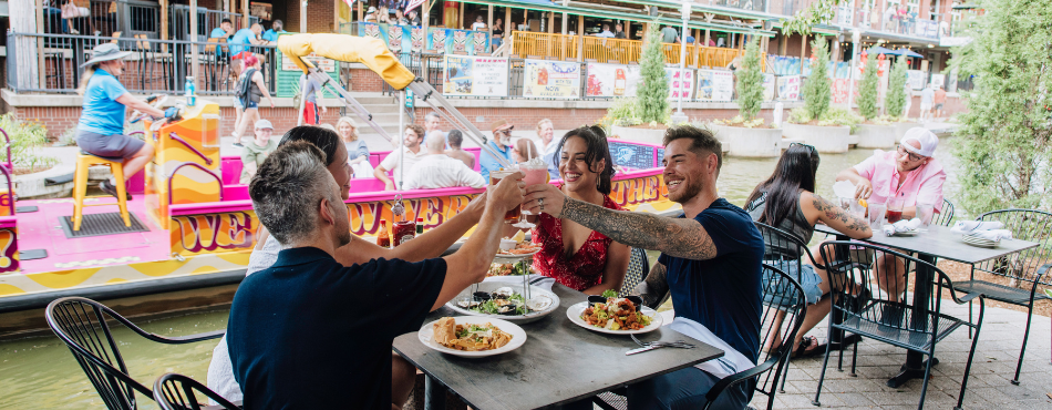 Two couples enjoying dinner as the Bricktown Water Taxi passes in the canal behind them