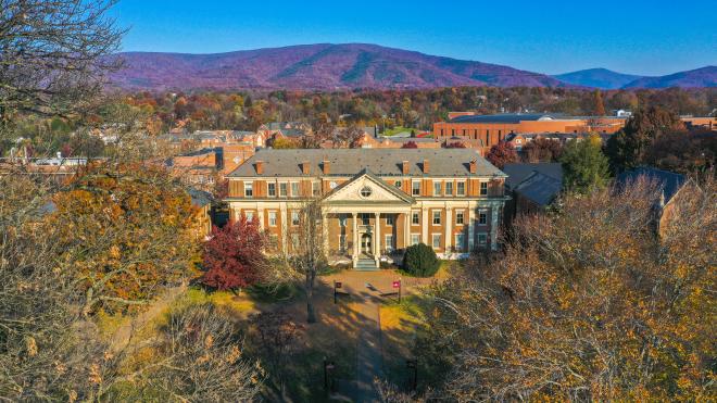 Aerial shot of the Roanoke College Administration building framed by fall color on trees in the foreground and fall color mountains in the background.