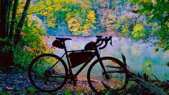 A bike sits in front of a misty lake surrounded by colorful fall trees and leaves.