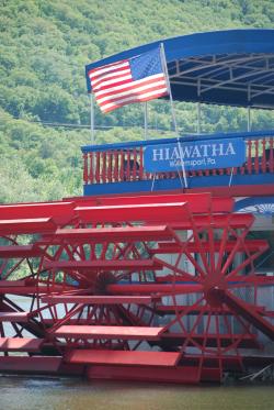 Picture of the Hiawatha paddle wheel boat on the Susquehanna River with an American flag attached to the boat and flowing on the wind.