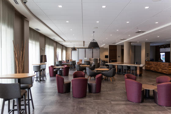 The main lobby filled with a mix of high-top tables and coffee tables with maroon colored chairs at the Courtyard by Marriott Elkhart