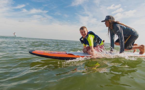 A child and instructor on a surfboard at Surfers Healing Team Camp Day in Virginia Beach