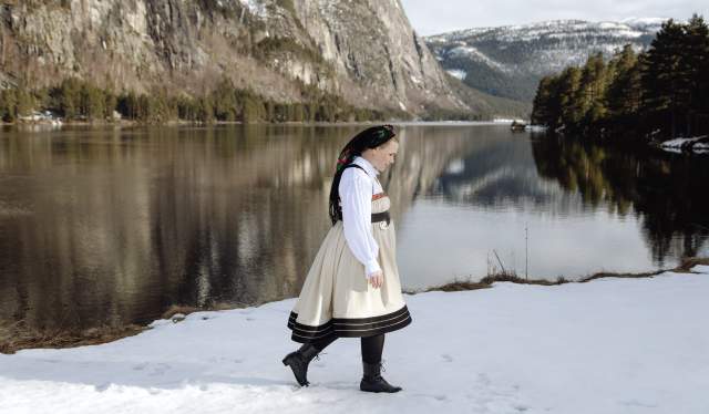 Young lady wearing national costume standing next to the river and steep mountains in Setesdal. Photo