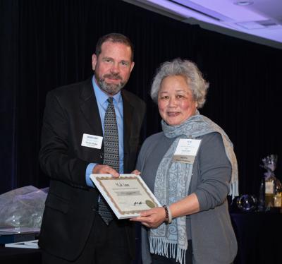 Yuk Lee, holding certificate for Behind-the-Scenes Award, next to Trevor Bridge, Chair of Board of Directors