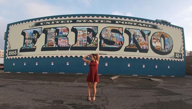 woman posing in front of fresno postage stamp mural
