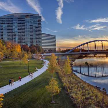 Orange and yellow trees surround the Scioto Mile and a sun sets in the background