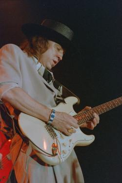 Photo of Stevie Ray Vaughan playing a guitar at an R and B Foundation Benefit he is wearing a dark colored hat and a light colored shirt