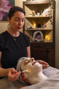 A serene spa setting featuring a facial treatment. A practitioner applies a mask to a client, surrounded by calming decor and soft lighting.