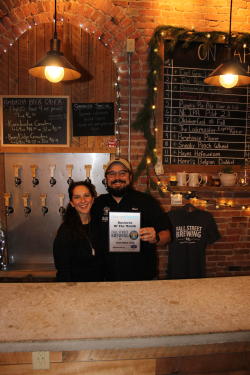 Fall Street Brewing Owners Brad and Anna Luisi-Ellis pose in front of the bar with their November 2020 business of the month plaque